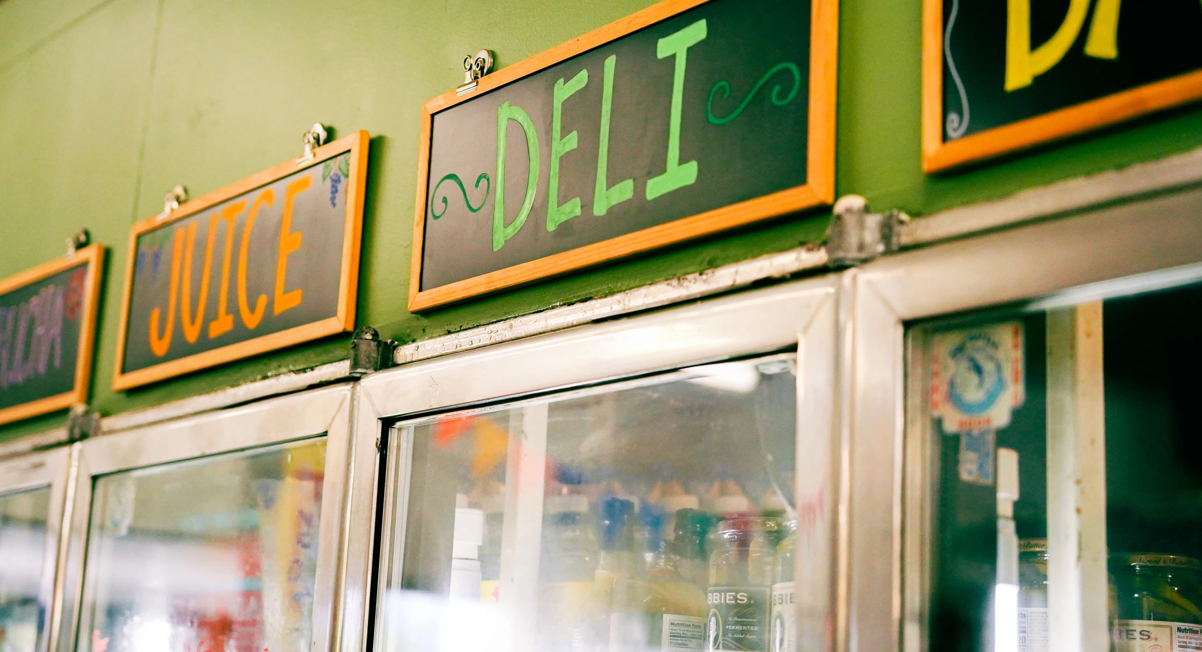Retail coolers labeled with hand-painted signs reading 'Juice' and 'Deli' hanging above the coolers.