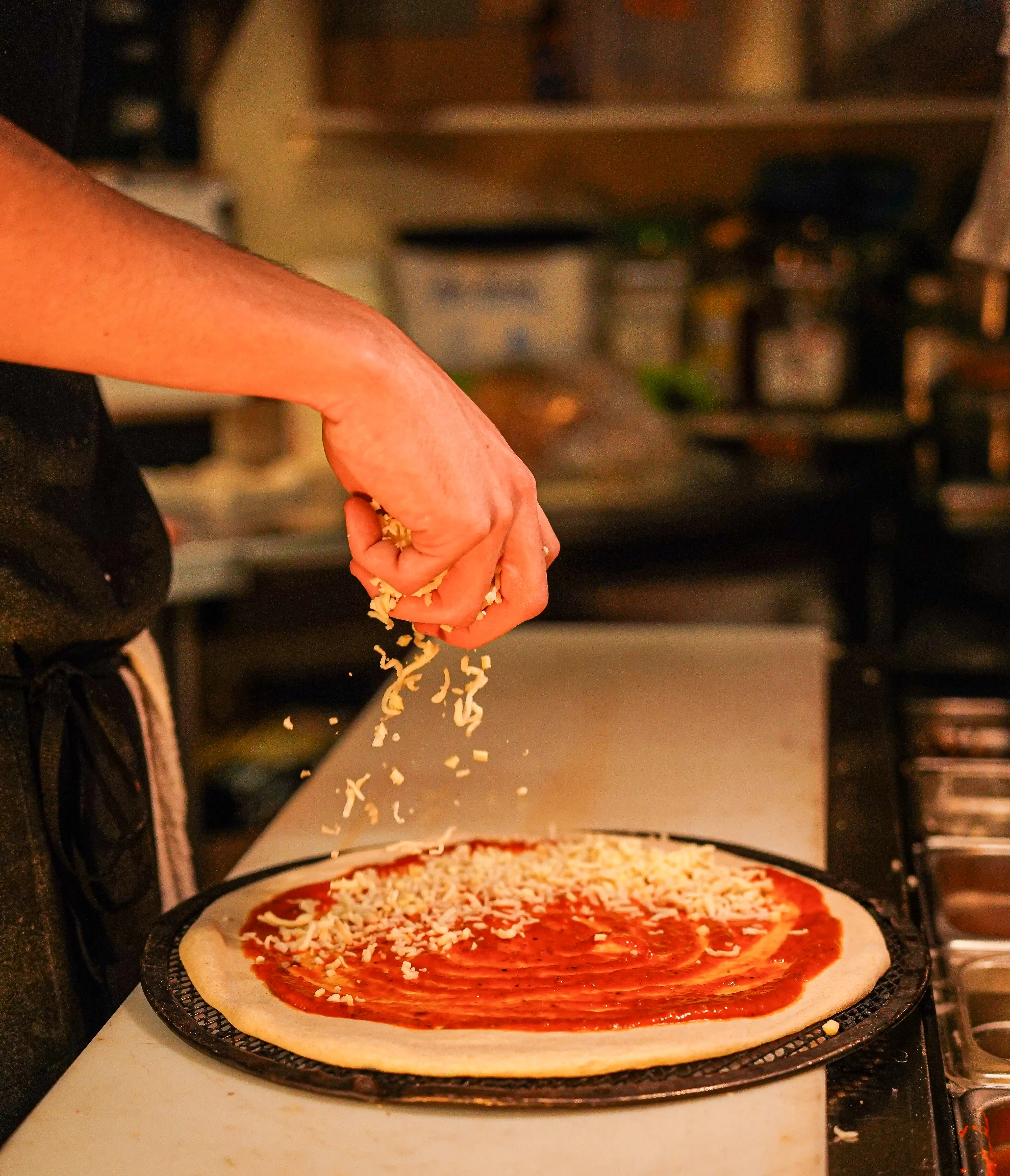 Shredded cheese being dropped on a red sauce pizza