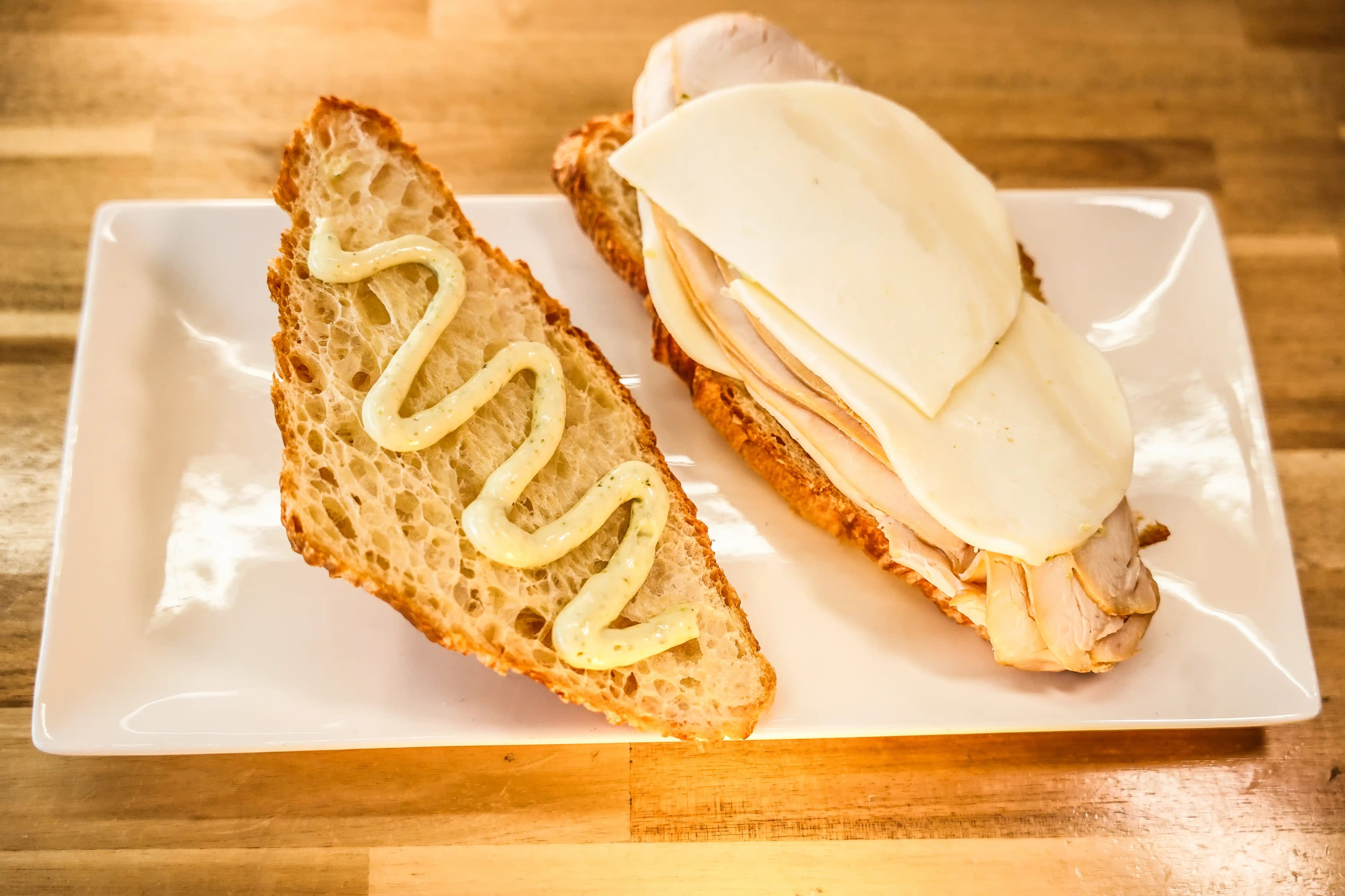 Open-faced turkey and provolone sandwich on croissant with a zigzag of aioli on the top slice, served on a white plate.
