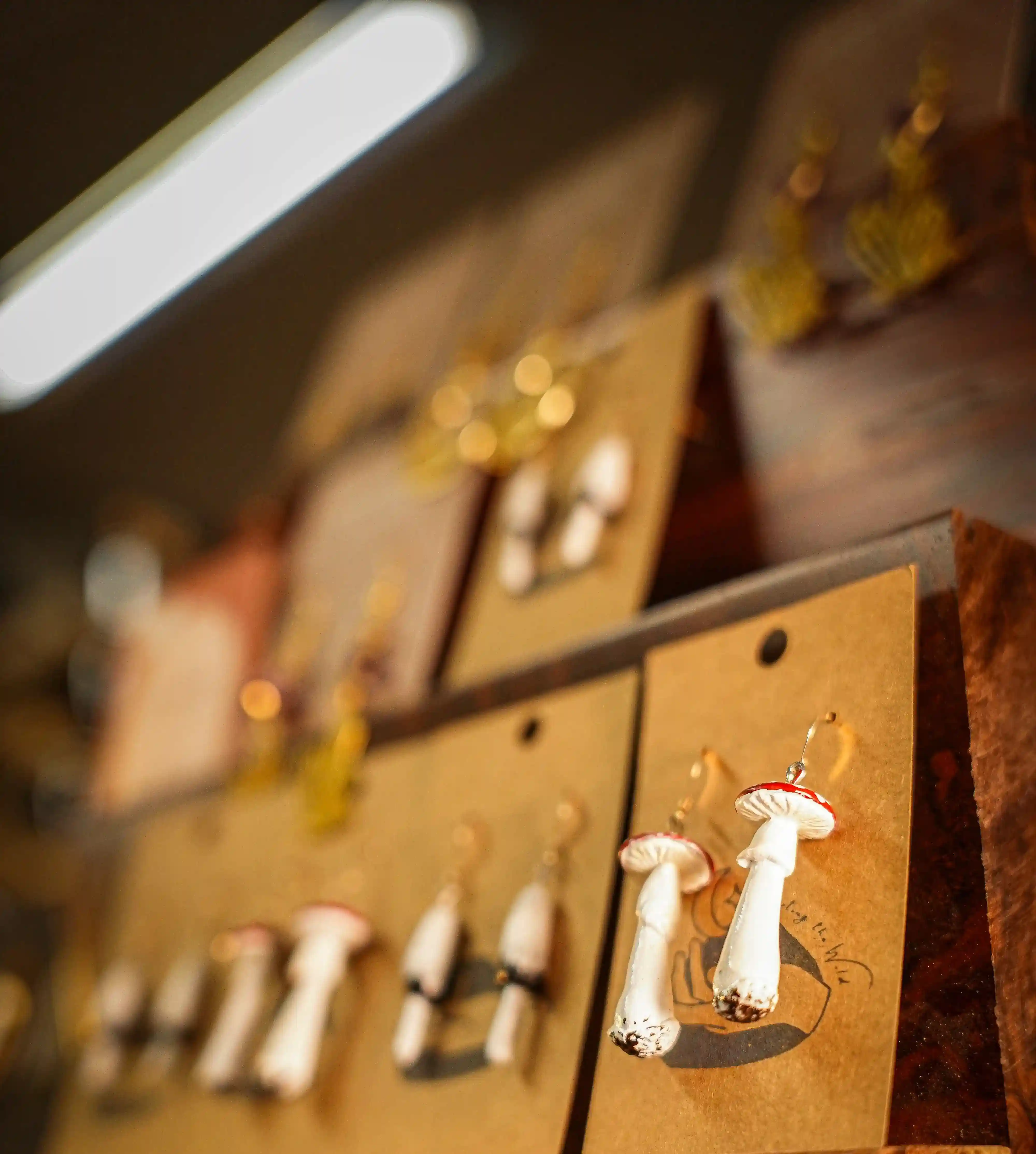 Handcrafted mushroom-shaped earrings displayed on brown cards in a wooden jewelry stand.