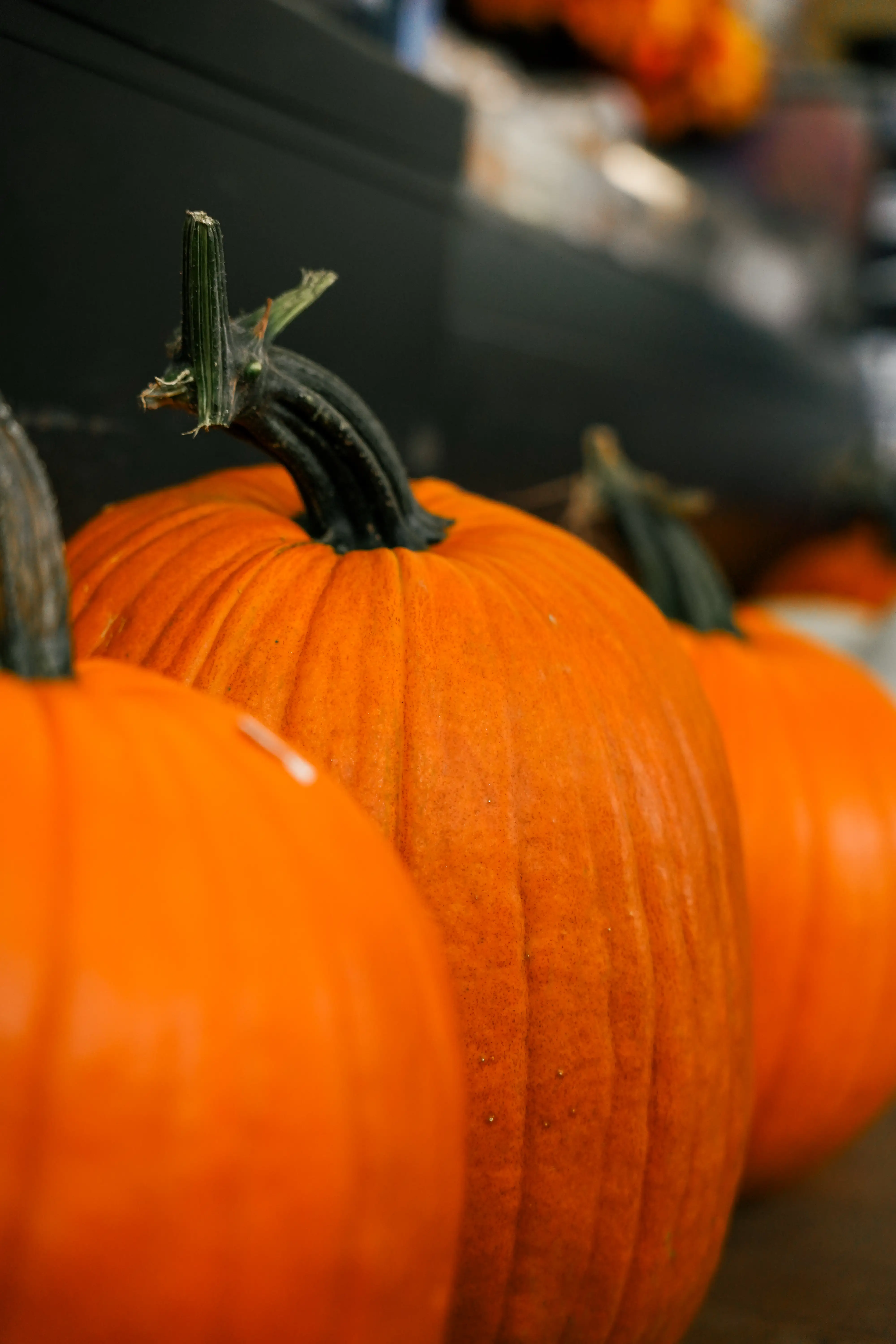 Close-up of bright orange pumpkins with dark green stems lined up on a market display.