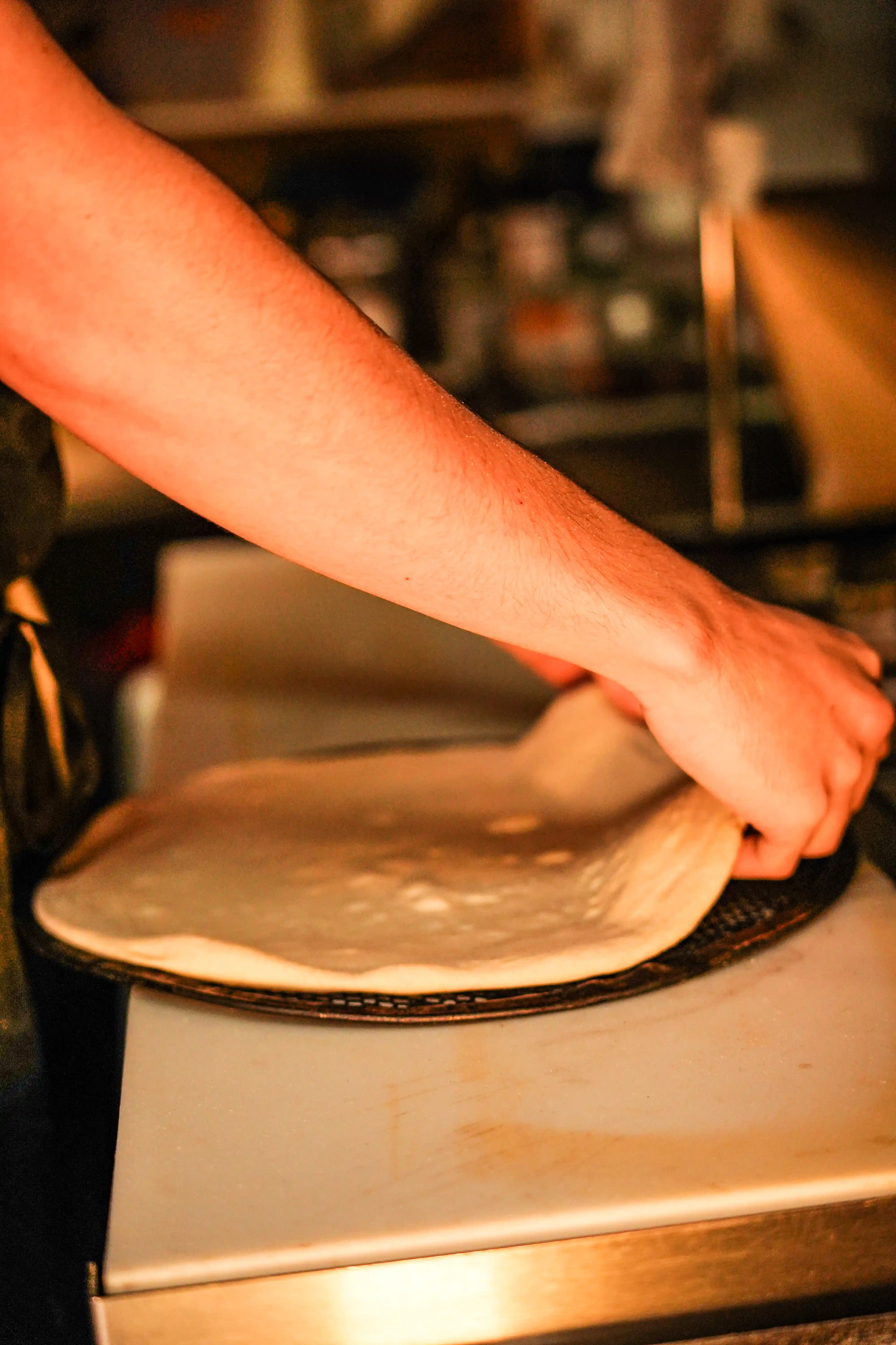 Two hands stretching pizza dough across a pizza screen.