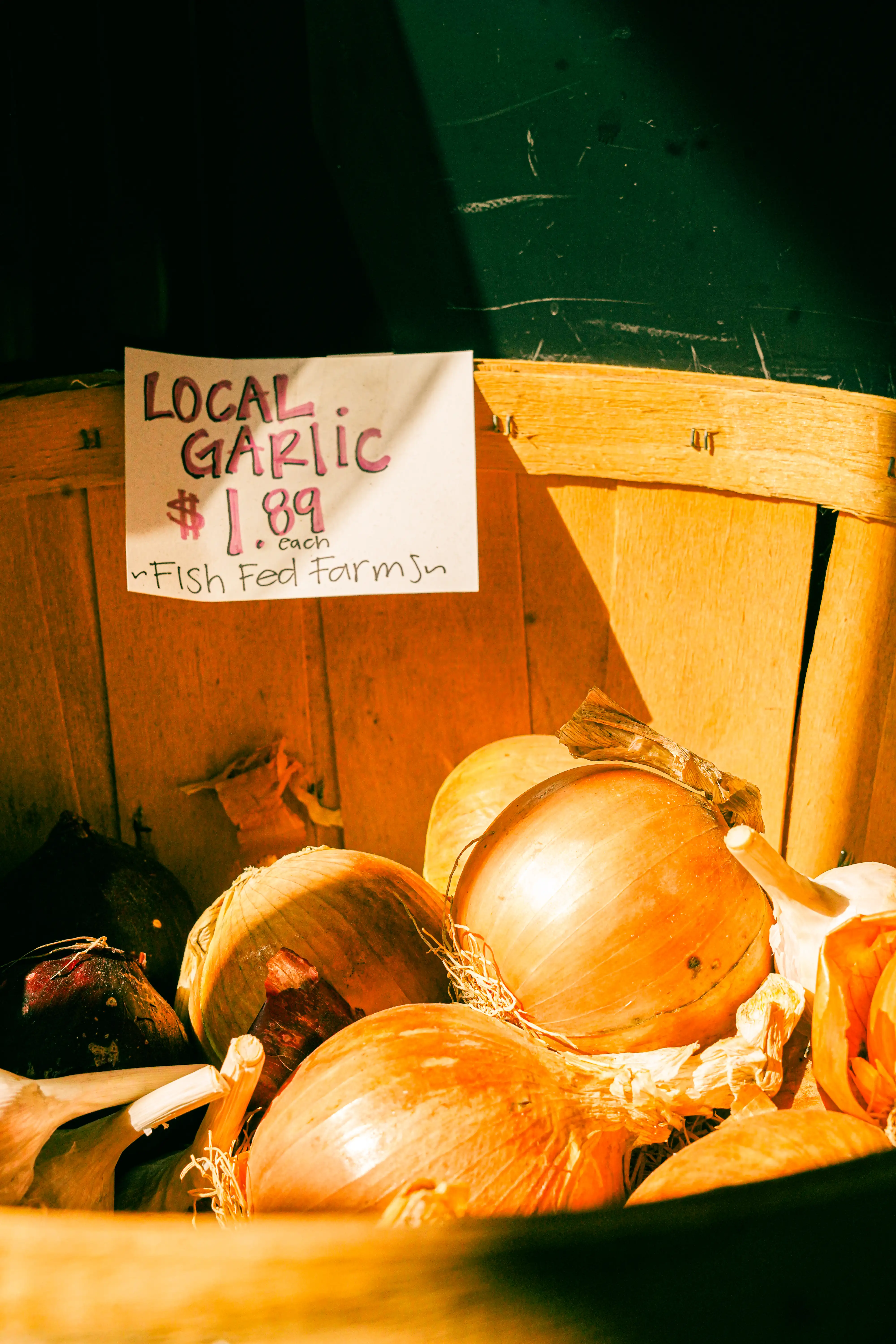 Basket of local garlic bulbs with a handwritten sign reading 'Local Garlic $1.89 each – Fish Fed Farms.'